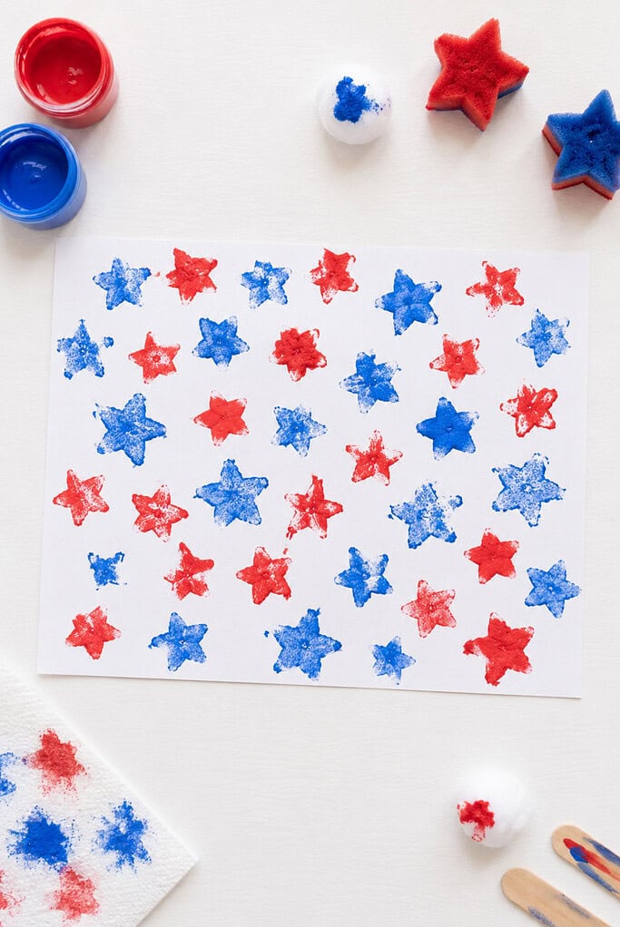a child's patriotic artwork created by stamping red and blue stars across a sheet of white paper using a cotton ball or star-shaped sponge dipped in paint.