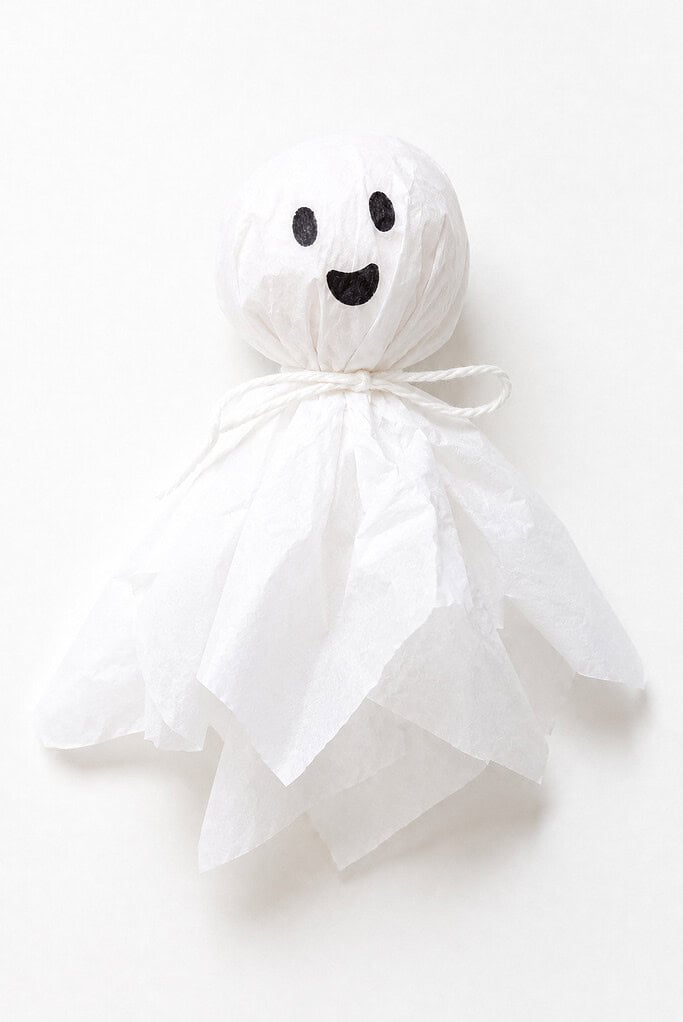 A white tissue paper ghost with a round ball head tied off with white string, black dot eyes and a small black smile drawn on the face, and flowing white tissue paper for the body