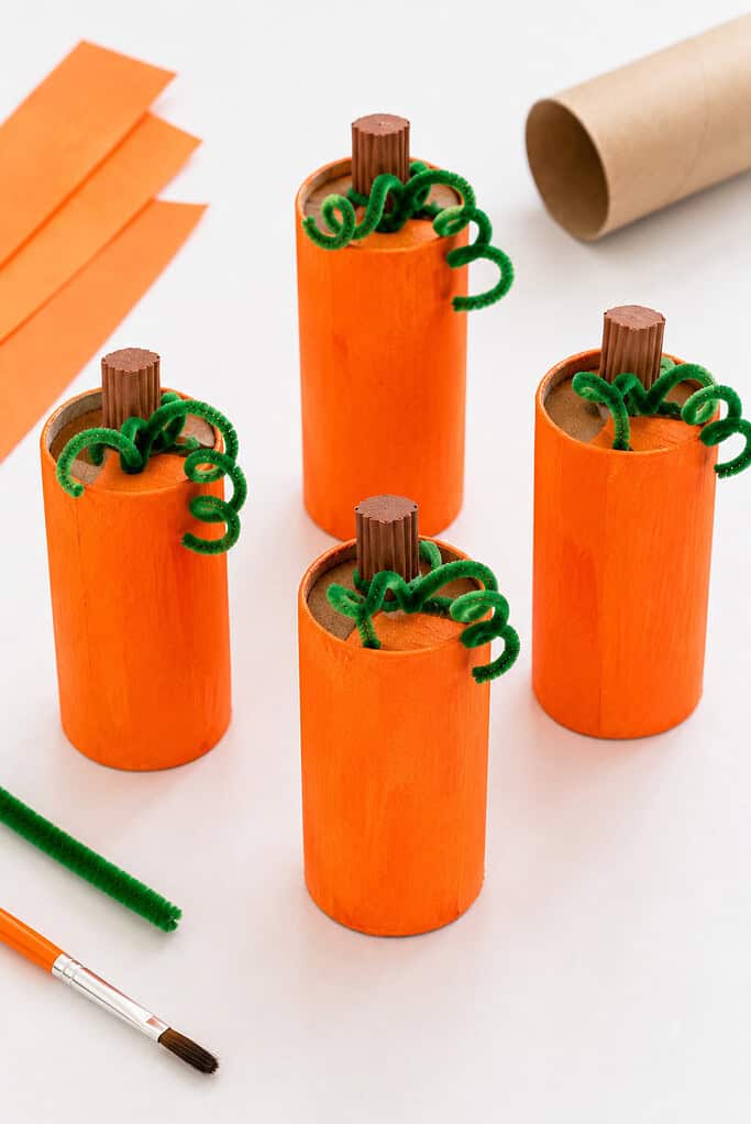 Several handmade pumpkins created from recycled cardboard toilet paper rolls wrapped in vibrant orange paper or painted bright pumpkin orange.