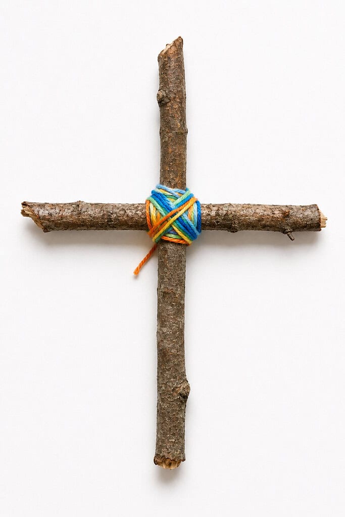 Two rough tree branches bound together in a cross shape with blue and orange yarn wrapped at the intersection