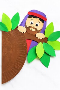 A paper craft featuring a smiling bearded figure with a purple robe and red headband, peeking over a brown painted paper plate tree trunk, surrounded by green paper leaves