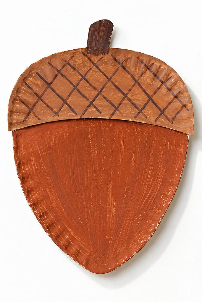 Painted paper plate cut into an acorn shape, with a dark brown stem, a tan cap marked with dark crosshatch lines, and a reddish-brown lower section on a white background.