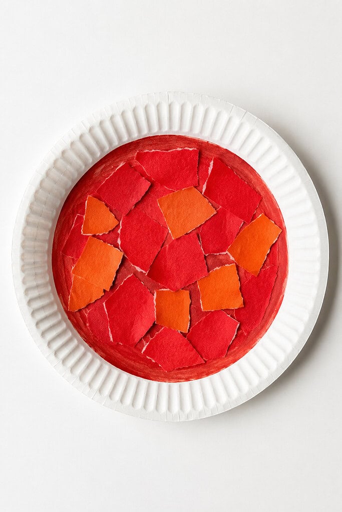 A white paper plate covered with torn pieces of red and orange paper.