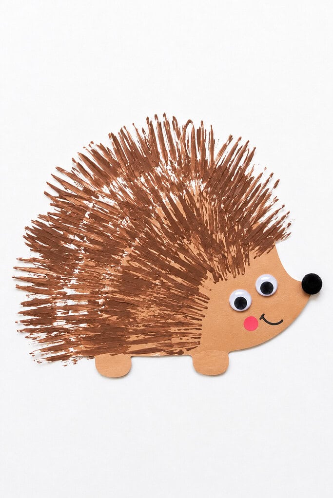 Brown fork-print marks covering the top of a paper hedgehog as spikes, over a tan body with googly eyes and a black pom-pom nose