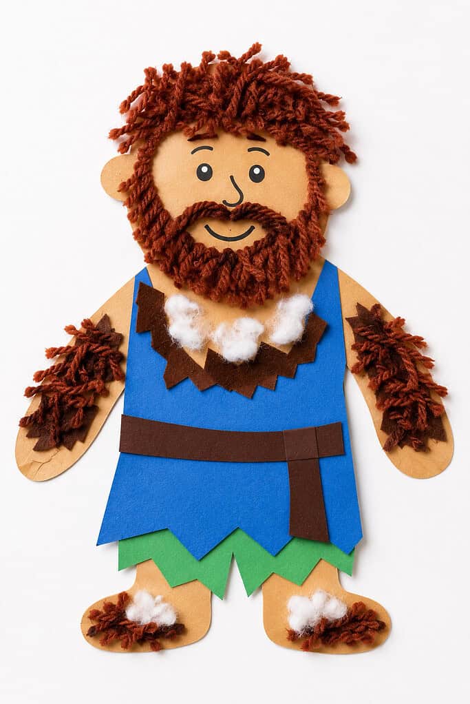 A paper figure with a face covered in brown yarn hair, beard, and mustache, wearing a blue paper tunic with a brown belt, a necklace of cotton balls, and matching yarn-covered paper arms.