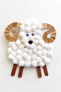 A fluffy cotton ball ram craft with curled paper horns, googly eyes, and paper legs on a white table.