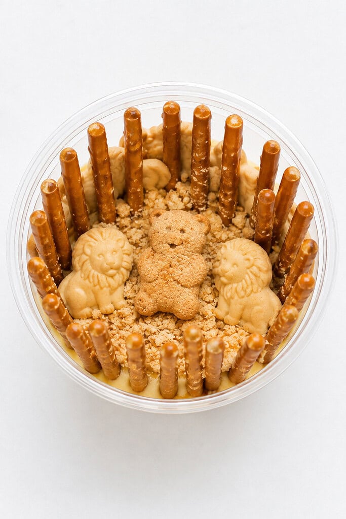 A clear cup with pudding, pretzel-stick den bars, lion crackers, and a teddy-bear graham for Daniel.