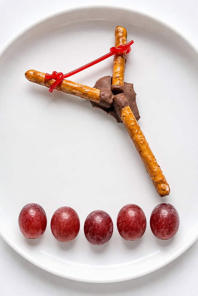 David and Goliath snack shaped like a slingshot from two pretzel rods with a red band and five grapes as stones.