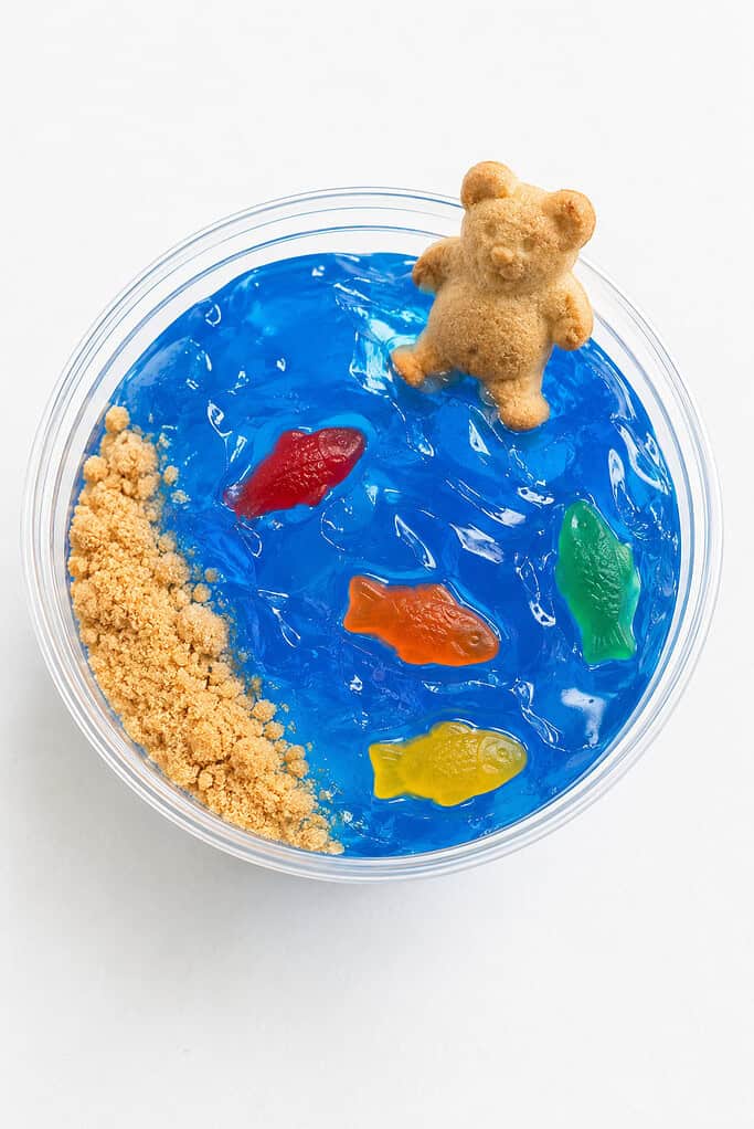 A clear cup of blue Jell-O with gummy fish and a teddy-bear cracker at the rim.