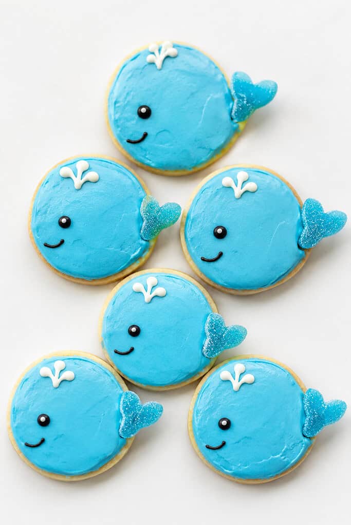 Round cookies iced blue like little whales with candy eyes and white frosting spouts.
