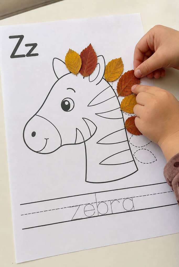 A child pressing a real leaf onto the guide of a leaf alphabet craft worksheet, with a few leaves already glued down