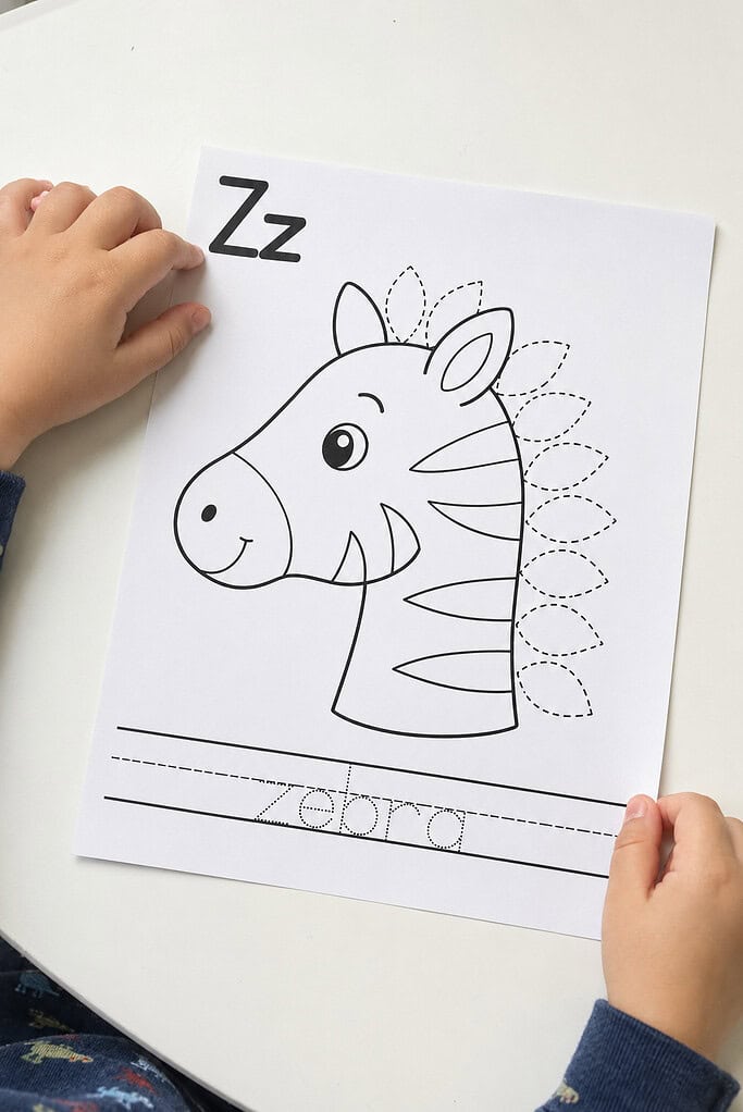 A child placing a printed black-and-white leaf alphabet craft worksheet on a white table