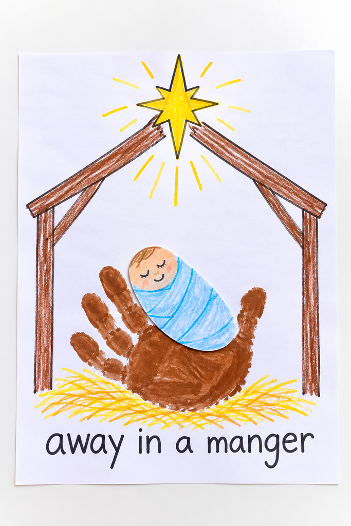 A brown handprint manger cradling a swaddled baby Jesus in the palm, with a star and away in a manger written below.