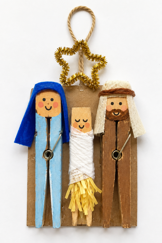 A clothespin nativity ornament of Mary, Joseph, and baby Jesus with a gold pipe-cleaner star and a twine loop.