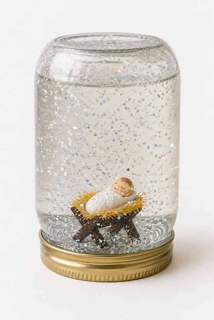 A homemade jar snow globe with a nativity figure inside and glitter snow swirling in the water.