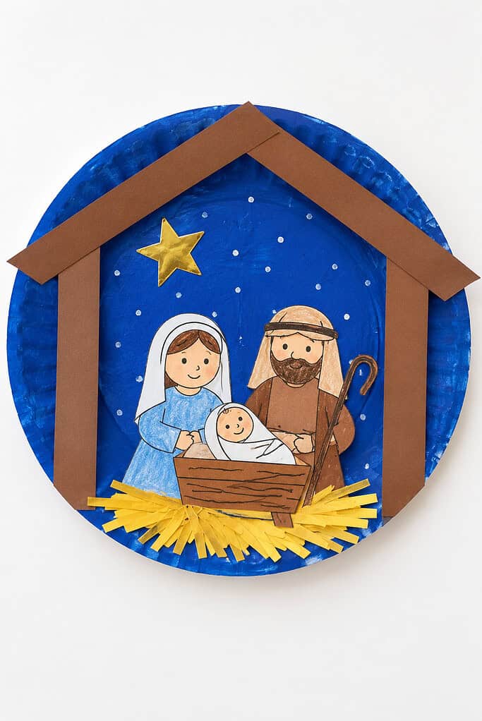 A paper plate nativity with a painted night sky, a stable roof, and cut-out Mary, Joseph, and baby Jesus.