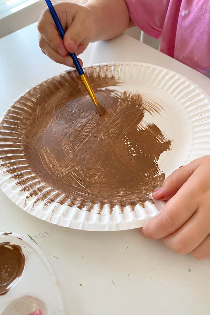 A child painting a paper plate brown to make the acorn body for the Nuts About Jesus acorn paper plate craft