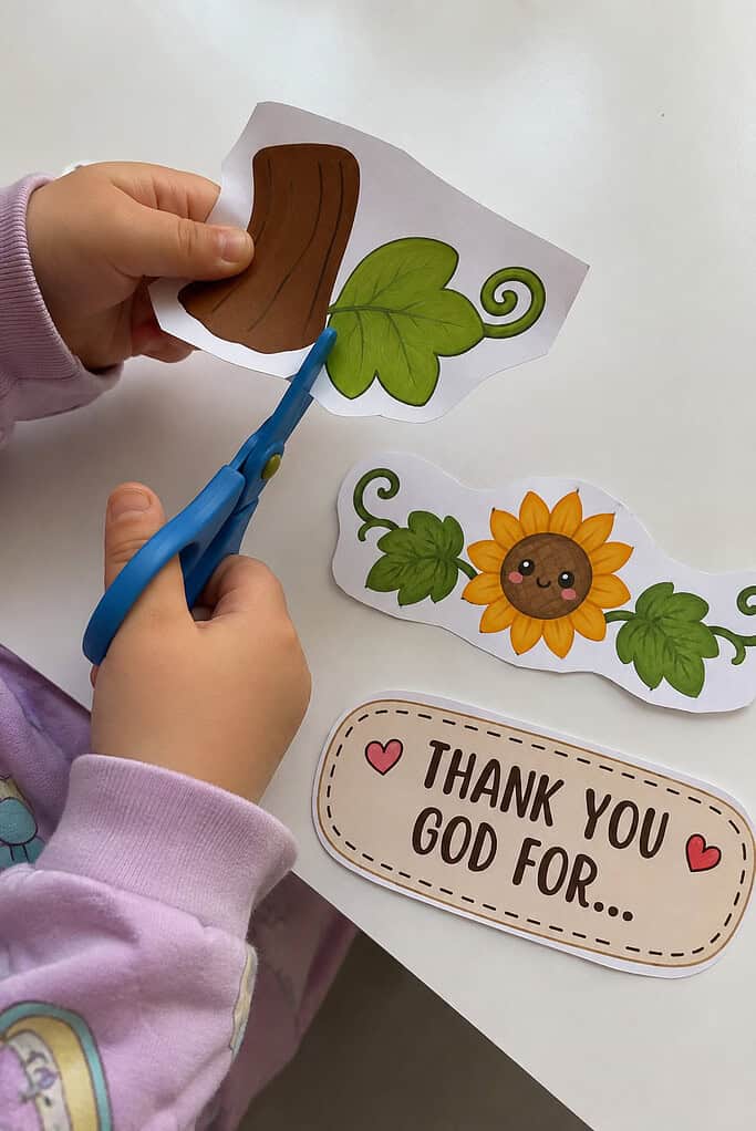 A child cutting out the printed pieces for a paper plate pumpkin Thanksgiving Bible craft with safety scissors