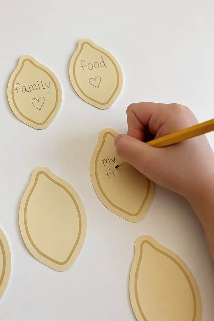 A child writing thankful words on the cream pieces for a paper plate pumpkin Thanksgiving Bible craft
