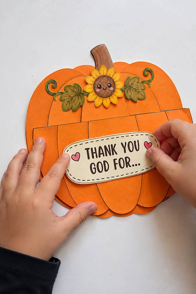 A child adding the "Thank You God For" sign and a sunflower to a Thanksgiving pumpkin Sunday school craft