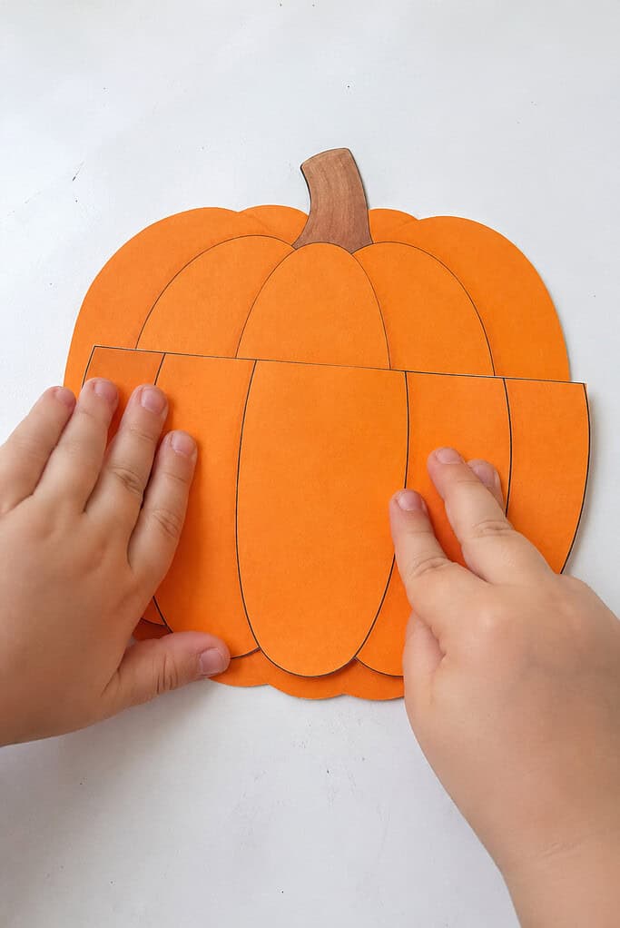 A child gluing the pumpkin base onto paper to form a pocket for a Thanksgiving pumpkin Sunday school craft