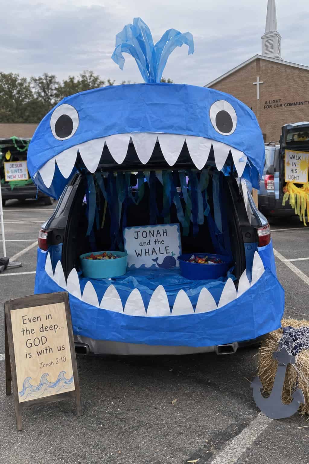 An open car trunk decorated as a big blue whale with a toothy mouth full of candy at a church trunk-or-treat.