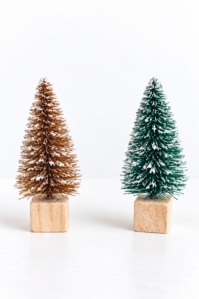 Small bottle brush Christmas trees on wooden block bases with twine, dusted with white snow.