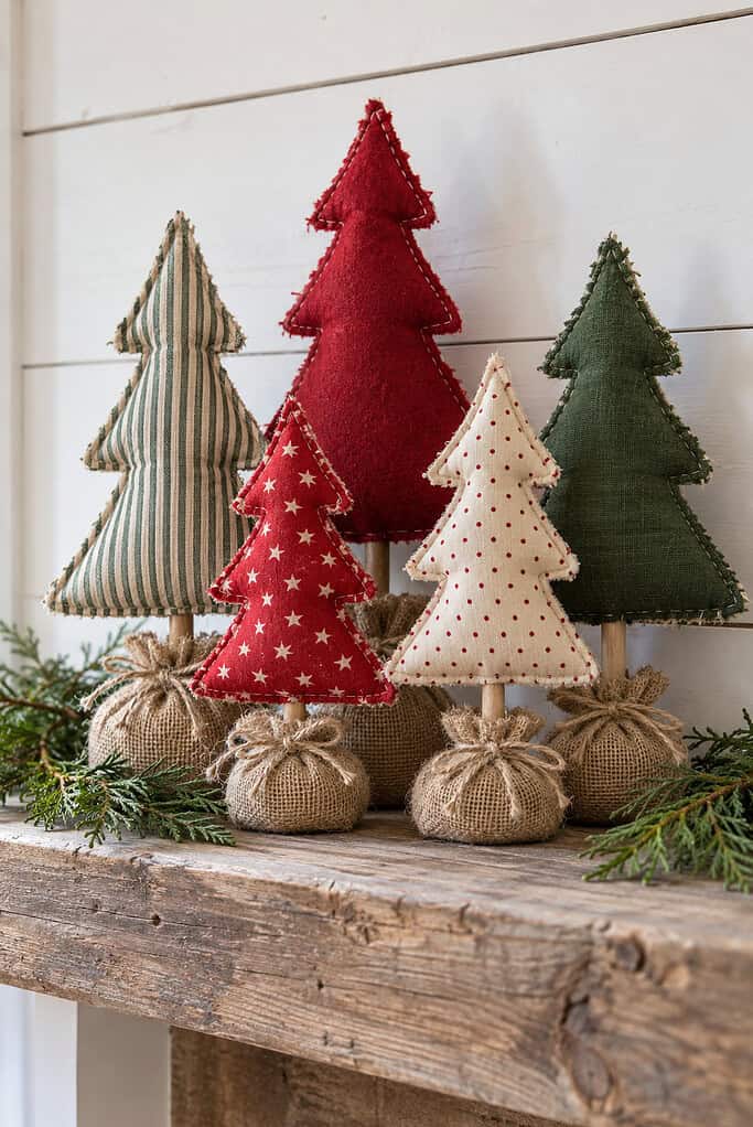 Five handmade stuffed fabric Christmas trees in red, green, stripe, and dot fabrics on wooden dowels with burlap bases, standing on a wooden mantel.