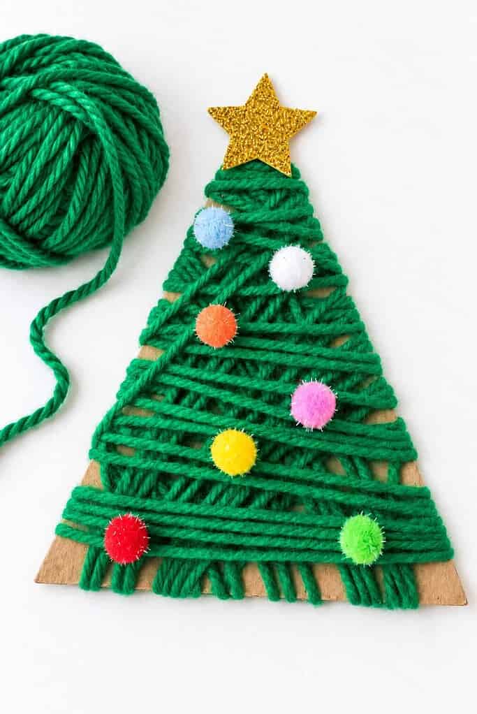 A green yarn-wrapped triangle Christmas tree with pom-poms and a gold star beside a ball of yarn.