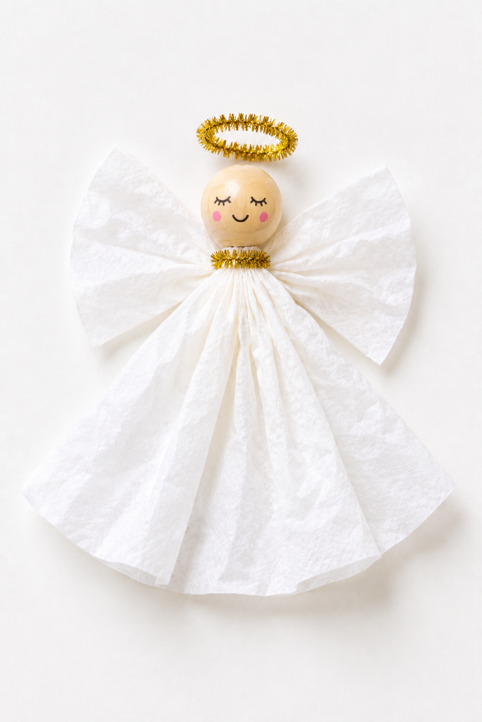 a coffee filter angel craft with a ruffled white gown, a bead head, folded filter wings, and a gold pipe cleaner halo on a white table