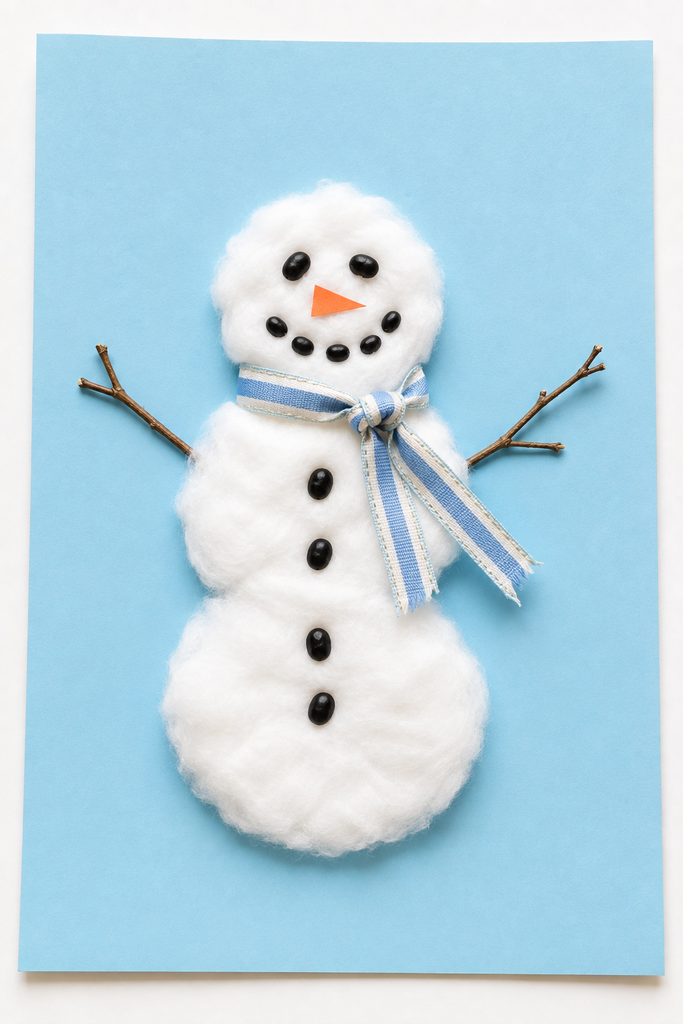 a fluffy cotton-ball snowman with twig arms and a ribbon scarf on light blue paper