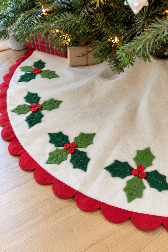 Cream fleece tree skirt with a red scalloped border and green felt holly sprigs with red button berries under a Christmas tree