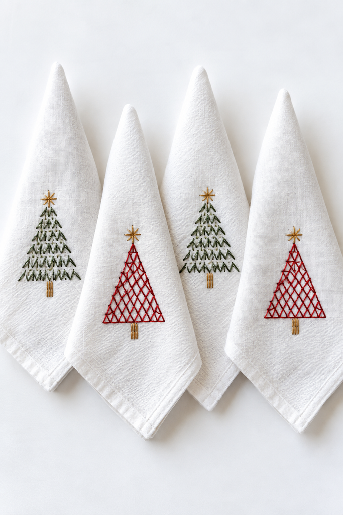White linen napkins folded into points, each with a small hand-embroidered red lattice or green Christmas tree
