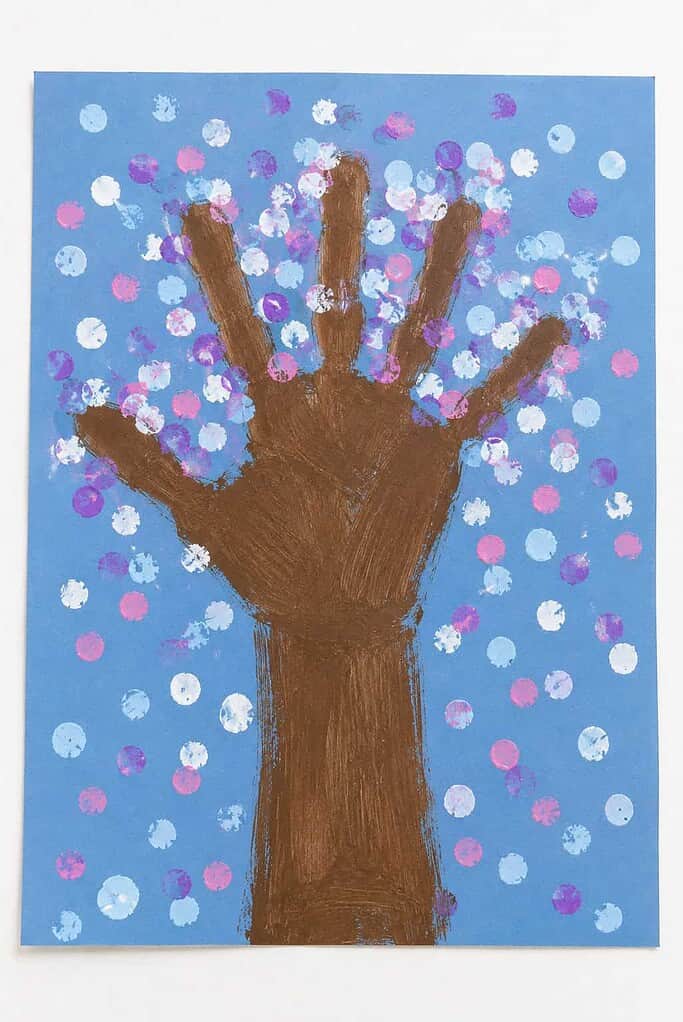 a brown handprint tree on blue paper surrounded by white, blue, and purple dotted snow