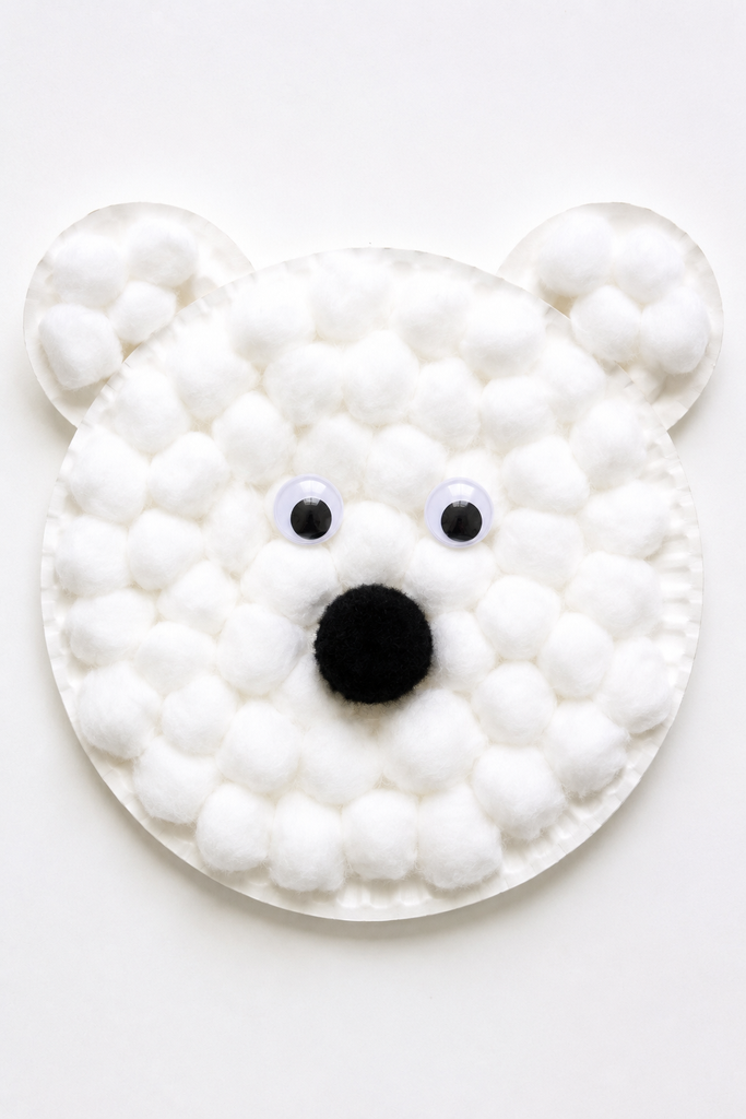 a paper plate polar bear face covered in cotton with googly eyes and a black pom-pom nose