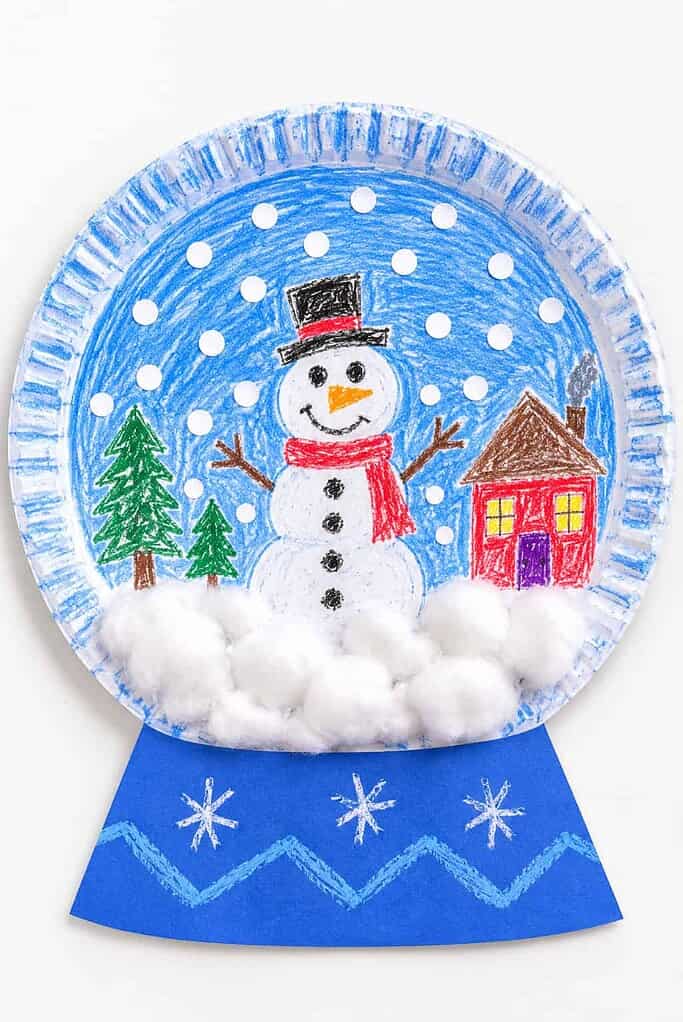 a paper plate snow globe with a crayon-drawn snowman scene, a paper base, cotton snow drifts, and paper dot snow