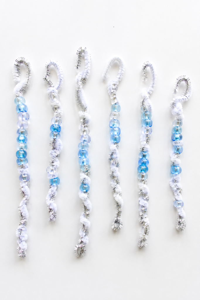 several pipe cleaner icicle crafts twisted into wavy spirals with clear and light blue beads and little hooks at the top on a white table