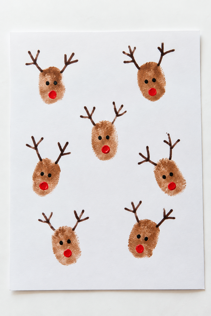 a card of small brown fingerprint reindeer with drawn antlers, dot eyes, and tiny red noses on a white table
