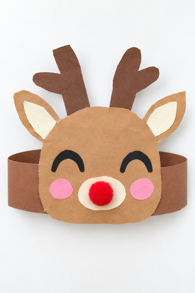 a wearable reindeer hat craft made from a brown paper headband with a reindeer face, ears, antlers, pink cheeks, and a red pom-pom nose on a white table