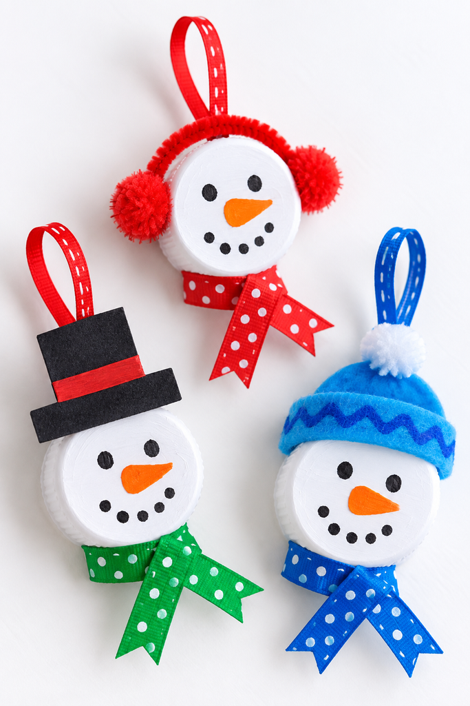 three bottle cap snowman ornaments, each a single white cap with a face, one with earmuffs, one with a top hat, and one with a hat, each with a scarf and hanging loop on a white table